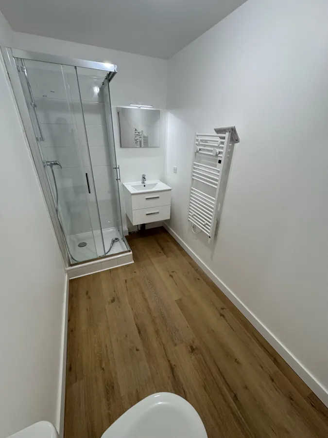 Salle d'eau après rénovation : cabine de douche vitrée, meuble vasque, sèche-serviettes et parquet