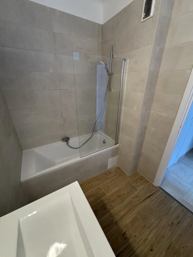 Baignoire neuve avec pare-baignoire vitré et carrelage beige après rénovation