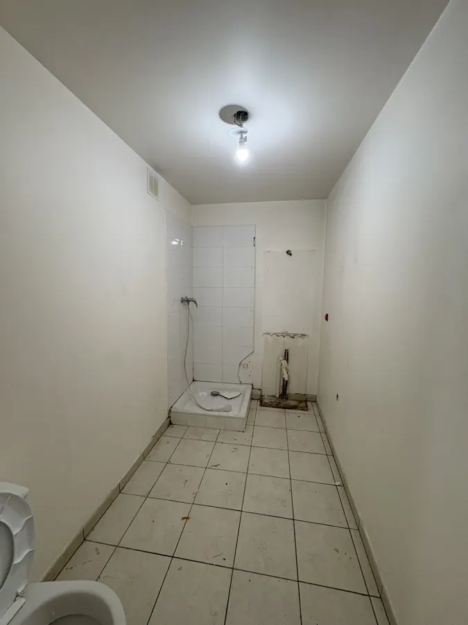 Salle d'eau avant travaux : receveur de douche nu, carrelage au sol, murs vides